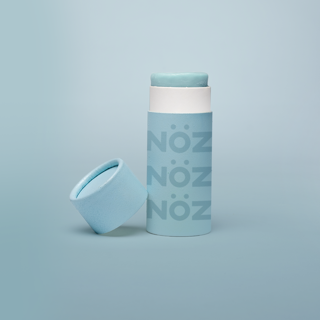 Blue Nözscreen sunscreen stick with lid to the left against a blue background 