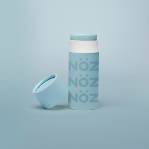 Blue Nözscreen sunscreen stick with lid to the left against a blue background 