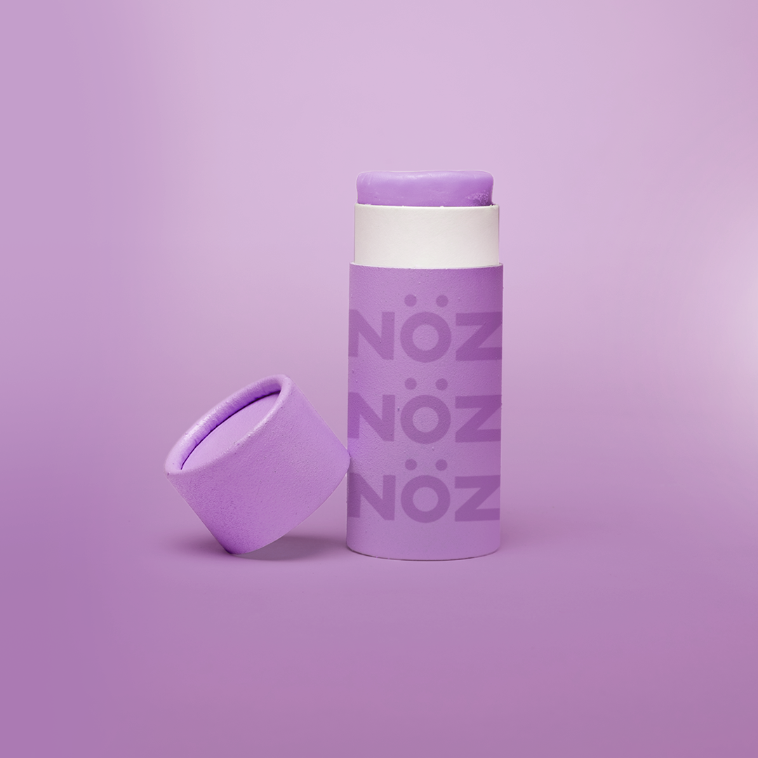 Purple Nözscreen sunscreen stick with lid to the left against a purple background 