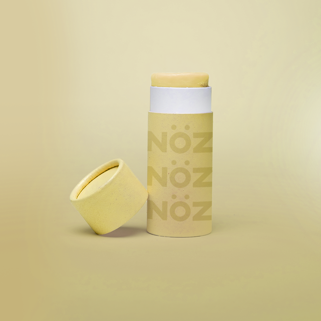 Yellow Nözscreen sunscreen stick with lid to the left against a yellow background 