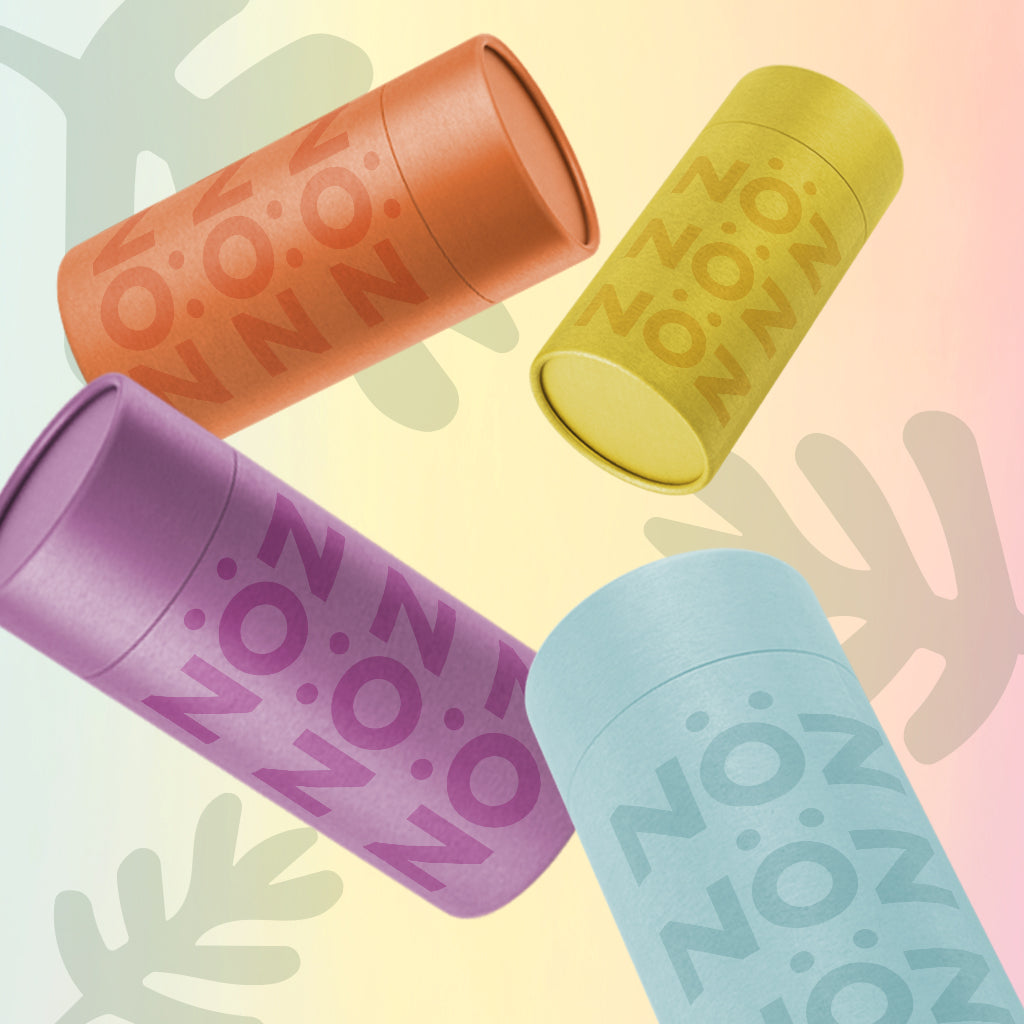 4 Nözscreen nose sunscreen sticks in orange, yellow, purple, and blue against a gradient yellow to pink background. 