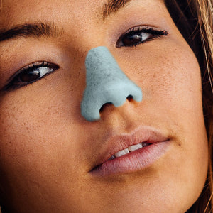 A woman with blue Nözscreen sunscreen painted on her nose. 